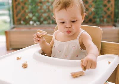 Baby sitzt in Hochstuhl und probiert Essen