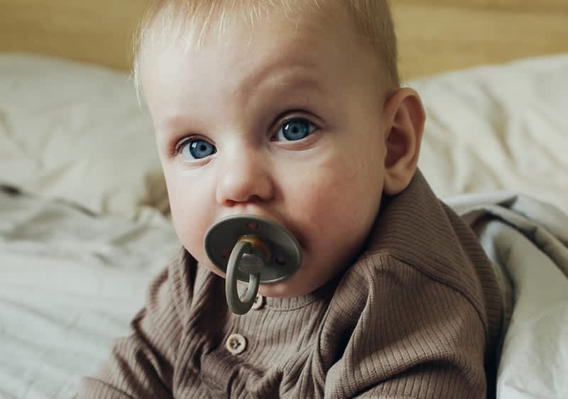 Baby mit olivgrünem Schnuller im Mund