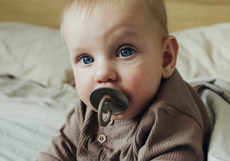 Baby mit olivgrünem Schnuller im Mund