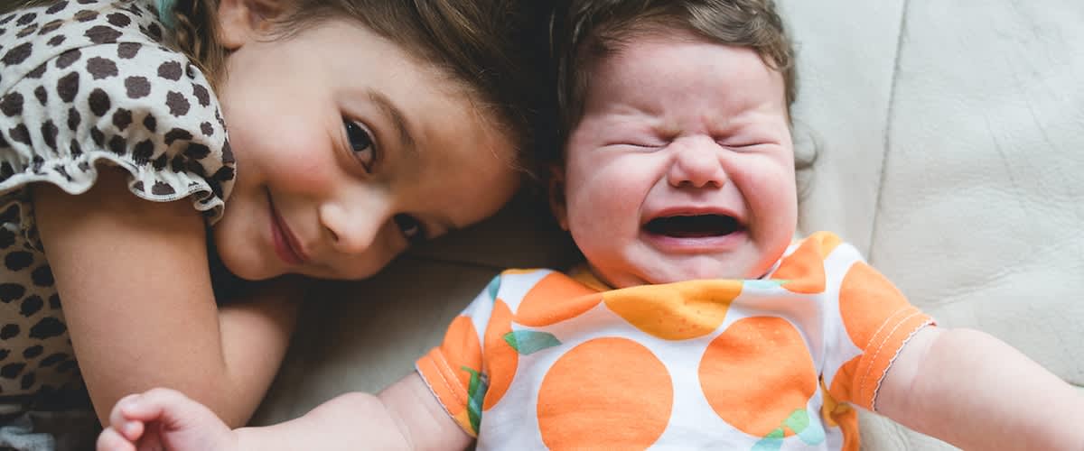 Lächelndes Mädchen liegt neben weinendem Baby