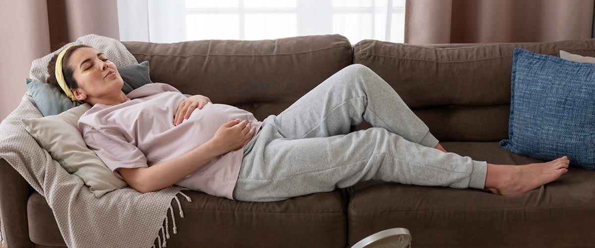 Schwangere Frau in Jogginghose liegt auf dem Sofa