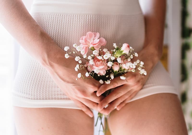 Frau hält Blumen vor ihrem Intimbereich
