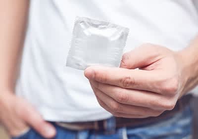 Mann mit weißen T-shirt haelt Kondom verpackt in der Hand