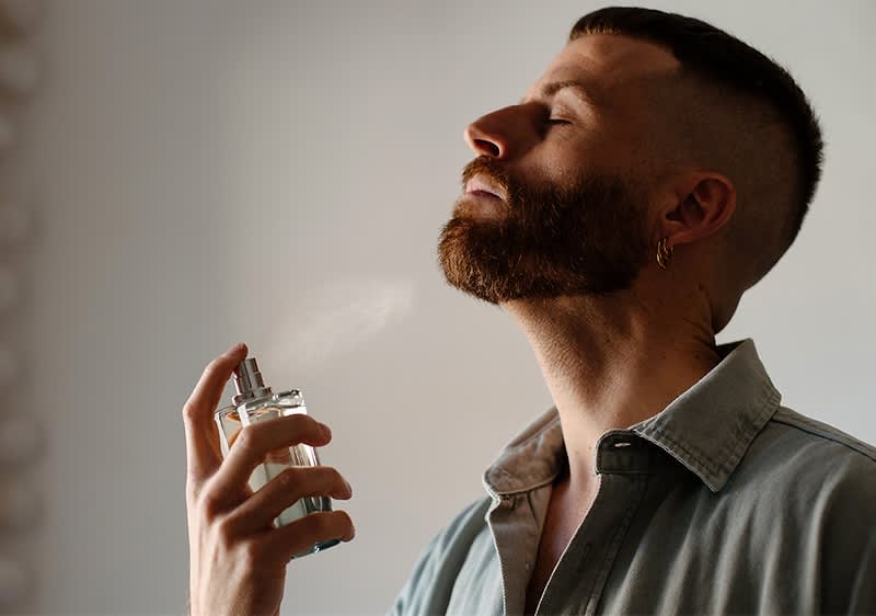 Mann bersprueht sich mit Parfum