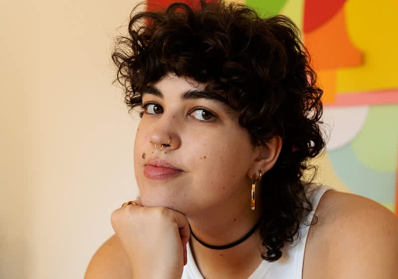 Person mit lockigem Haar vor buntem Wandbild