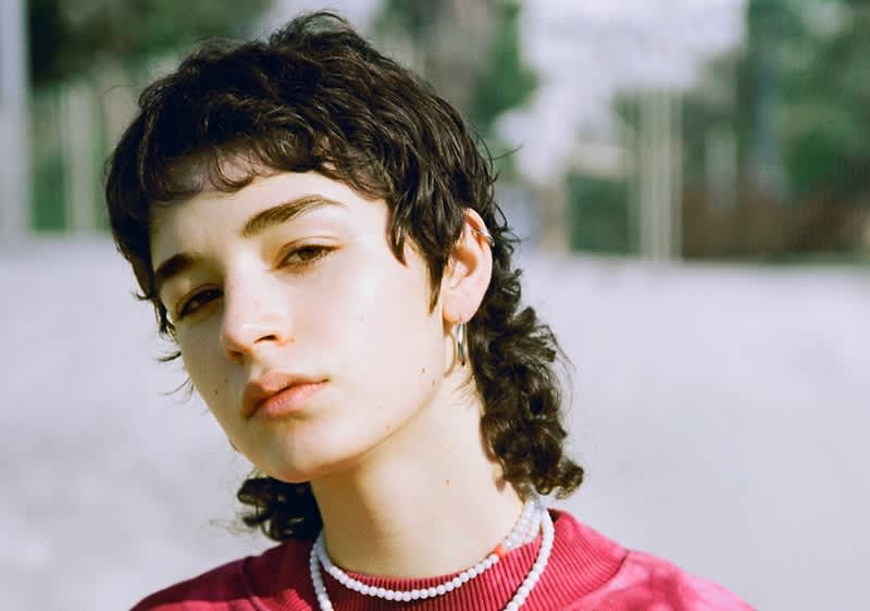 Person mit lockigem Haar und rotem Pullover im Freien