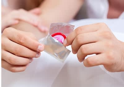 Kondom in geöffneter Verpackung in Händen gehalten