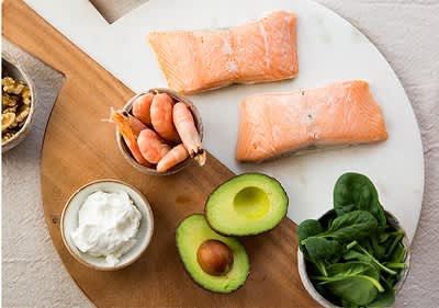 Gesunde Lebensmittel: Lachs, Garnelen, Avocado, Spinat, Walnüsse, Frischkäse auf Holzbrett