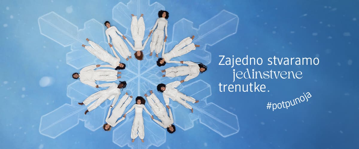 Acht Personen in weißen Anzügen liegen kreisförmig auf einem blauen Hintergrund mit Schneeflockenmuster, daneben der Text „Gemeinsam sind wir einzigartig“ und „#ganzich“