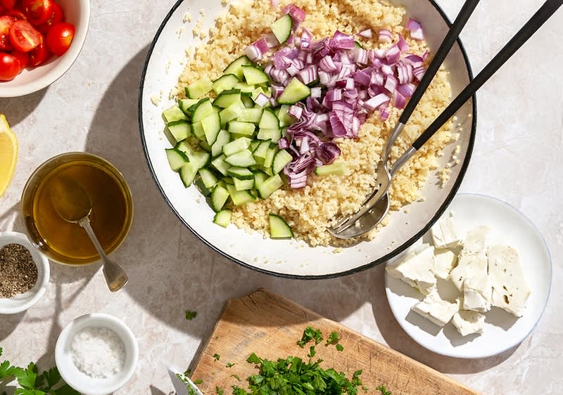Sastojci za salatu uključuju kuskus, krastavac, crveni luk, paradajz, feta sir i začine.