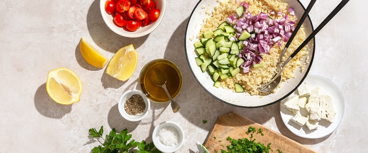 Sastojci za salatu uključuju kuskus, krastavac, crveni luk, paradajz, feta sir i začine.