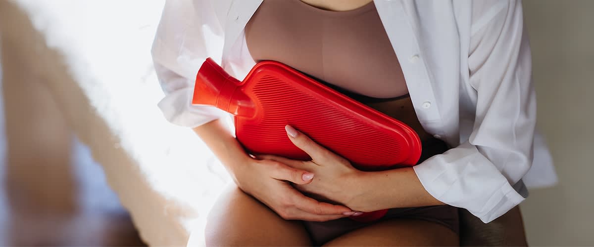 Žena sa flašom za toplu vodu na stomaku, u donjem vešu i košulji