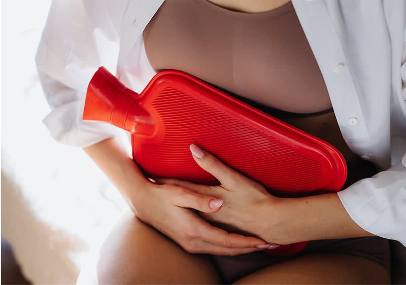 Wärmflasche auf Bauch einer Frau in Unterwäsche und Hemd