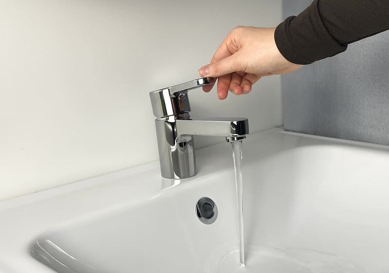 Ruka podešava slavinu iz koje teče voda u lavabo