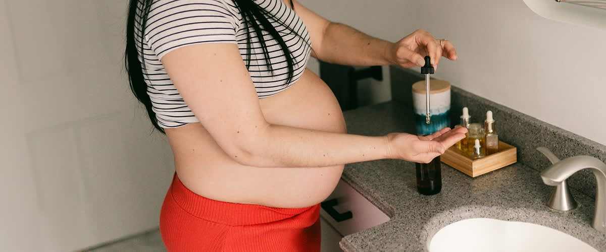 Slika koja prikazuje trudnu ženu sa izloženim stomakom kako koristi pipetu iznad bočice