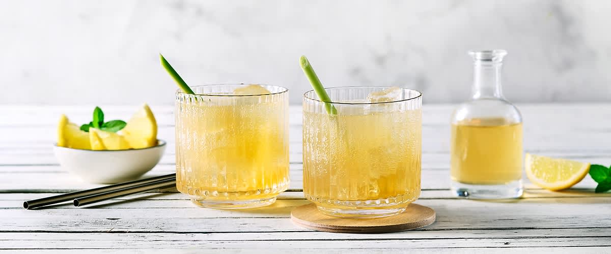 Zwei Gläser Sommerspritz mit Eis und Zitronengras auf Holztisch