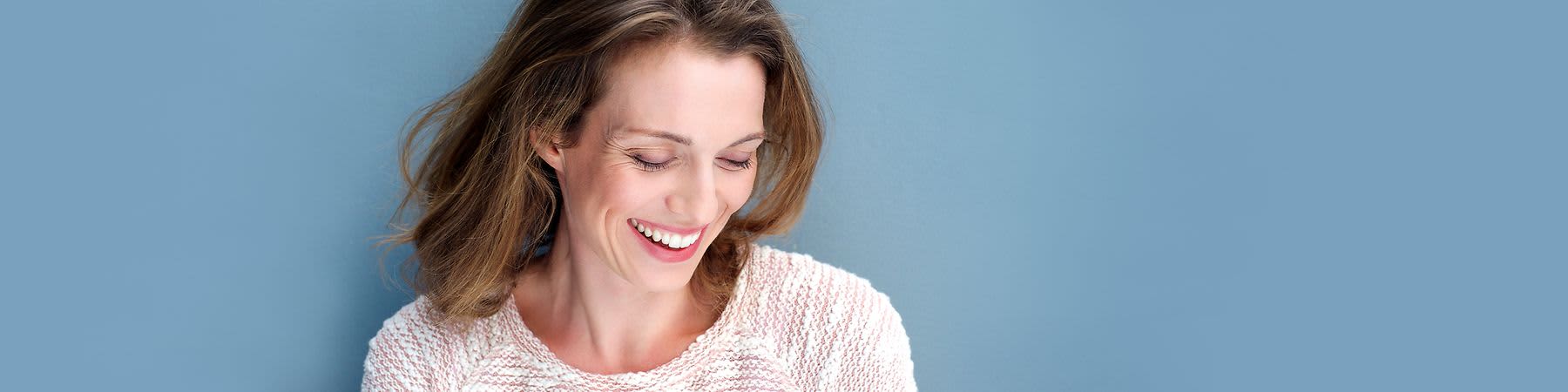 Lachende Frau mit Blick nach unten auf blauem Hintergrund