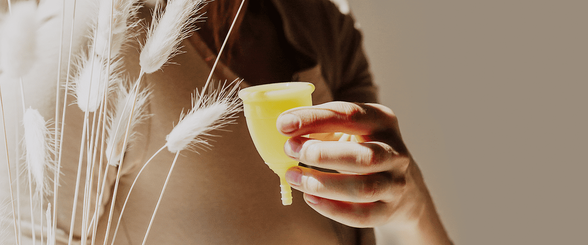 Hand hält gelbe Menstruationstasse