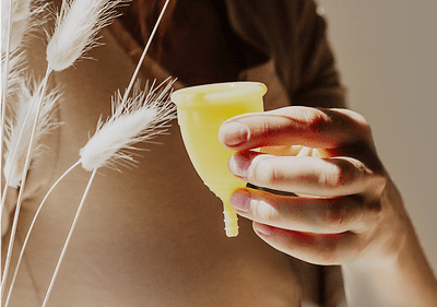 Hand hält gelbe Menstruationstasse
