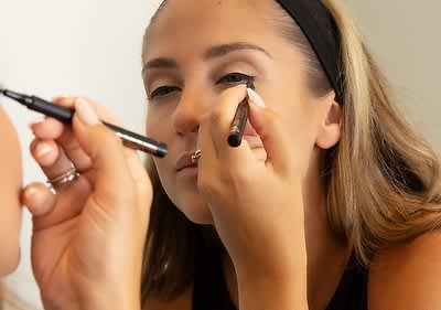 Alt-Text: Ličenje z eyelinerjem na očesu ženske z dolgimi svetlimi lasmi