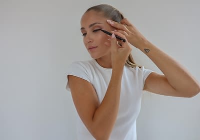 Alt-Text: Ličenje z eyelinerjem na očesu ženske z dolgimi svetlimi lasmi